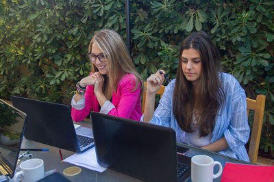 Female colleagues using laptop against plants