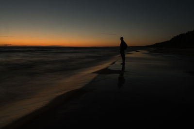 Silhouette man standing on beach against sky at sunset