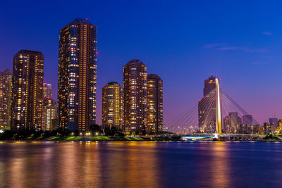 Illuminated city by river against sky at night