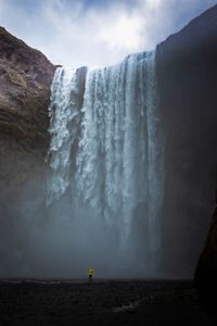 Distant view of person standing against waterfall against sky
