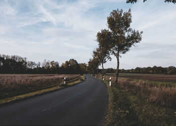 Empty road amidst field against sky