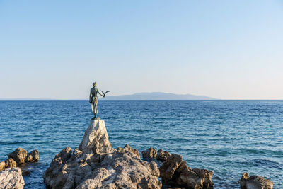 Man standing on rock by sea against clear sky