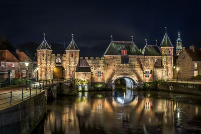 Illuminated bridge over river against buildings at night