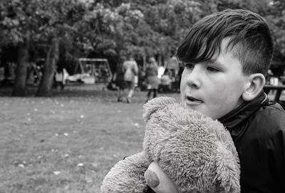 Boy looking away while holding teddy bear in park