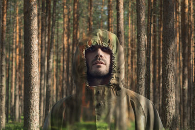 Portrait of young man standing by tree trunk in forest