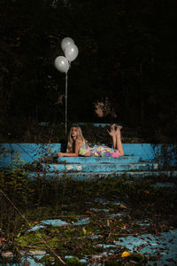 Portrait of young woman with helium balloons relaxing in park at night