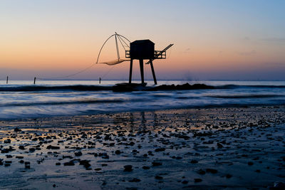 Silhouette parasols on beach against sky during sunset