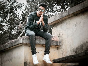 Full length of young man wearing sunglasses while sitting on terrace against trees