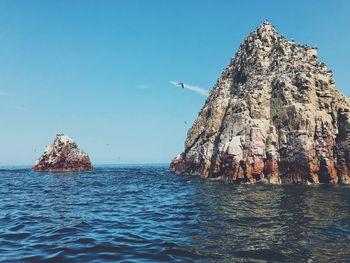 View of rock formation in sea against clear blue sky