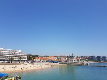 View of buildings by river against blue sky