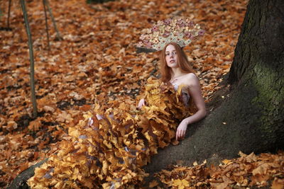Young woman wrapped in autumn leaves against tree