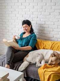 Young woman with dog sitting against brick wall