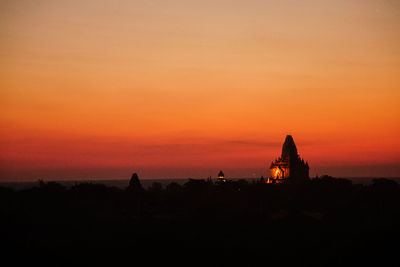 Silhouette temple against building during sunset