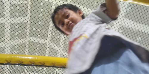 Rear view of boy playing with chainlink fence