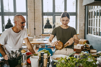 Male colleague looking at female chef preparing food in studio