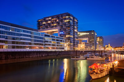 Boats moored in canal by illuminated buildings against sky at night