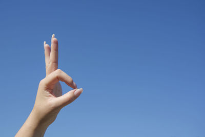 Cropped hand of woman gesturing ok sign against clear blue sky