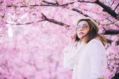 Woman in sunglasses standing against pink cherry blossom tree