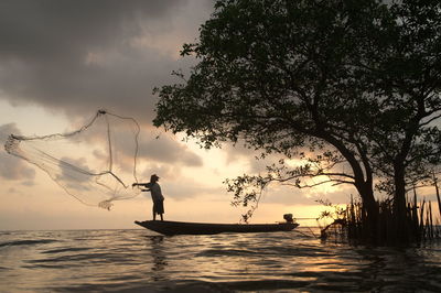 Man fishing in sea against sky during sunset