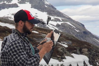 Young man photographing while standing against mountain during winter