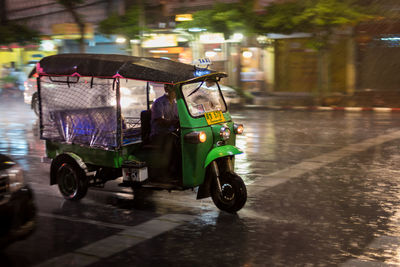 Man driving tuk-tuk on road at night during rain