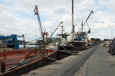 Boats in harbor against cloudy sky