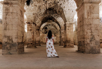 Rear view of female tourist standing in large underground room of an ancient roman palace in split