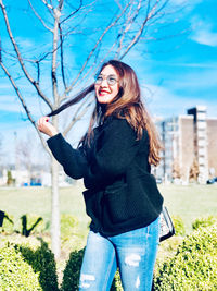 Side view of young woman standing against tree