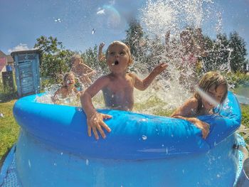 Children playing with water in wading pool against sky