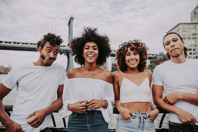 Cheerful friends standing against bridge in city