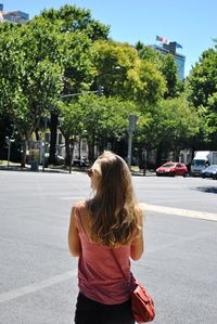 Rear view of woman standing on road against trees