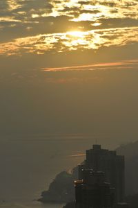 Silhouette cityscape by sea against sky during sunset