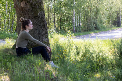 Young brunette woman sitting in green forest enjoys the silence and beauty of nature 