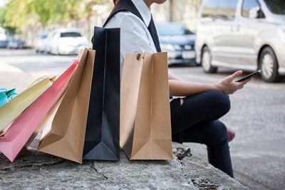 Midsection of person sitting with shopping bags on sidewalk