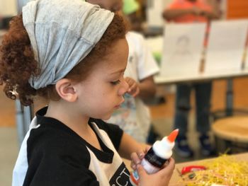 Close-up of girl in headwear holding bottle while sitting indoors