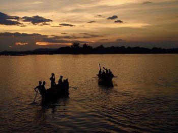 Silhouette people in boat against sky during sunset