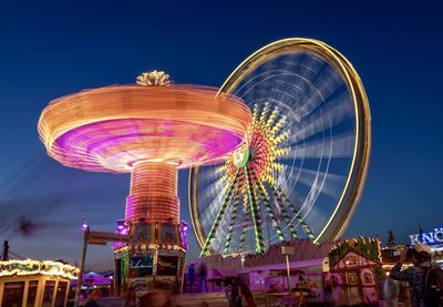 Illuminated amusement park rides spinning against sky at night