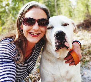 Portrait of smiling woman wearing sunglasses with dog in forest