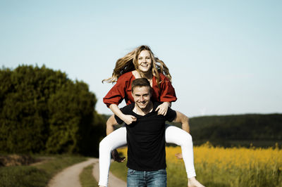 Portrait of man piggybacking woman on road against sky