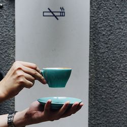 Cropped image of hand holding coffee cup against wall