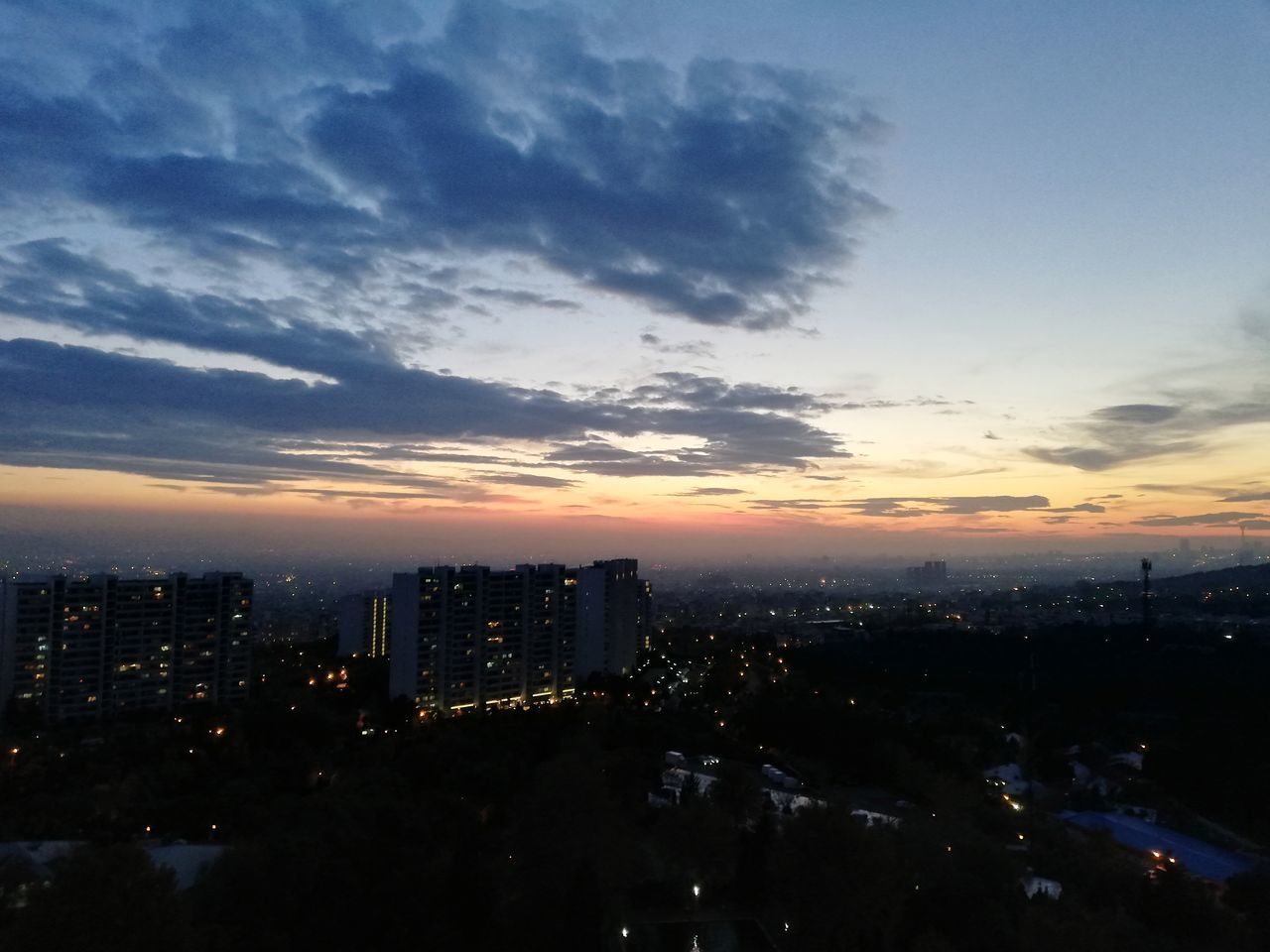 HIGH ANGLE VIEW OF ILLUMINATED BUILDINGS IN CITY AGAINST SKY