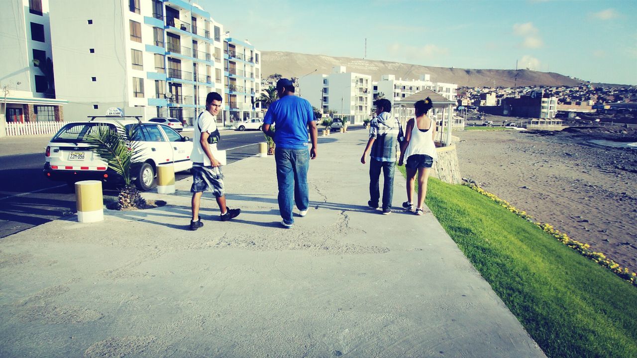 lifestyles, men, full length, leisure activity, walking, building exterior, togetherness, sky, architecture, person, built structure, rear view, casual clothing, beach, sunlight, boys, bonding