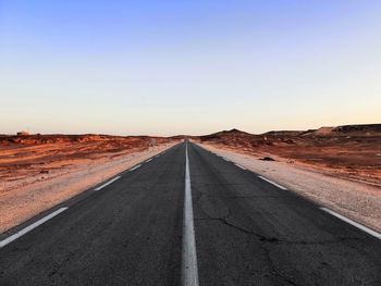 Diminishing perspective of empty road at desert against clear sky