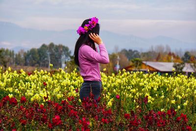 Side view of woman standing amidst flower against sky