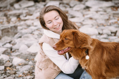 Young woman and dog retriever walks on river shore at autumn season