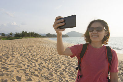 Portrait of smiling young woman using phone on beach