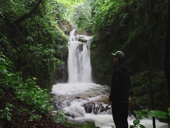 Rear view of man standing against waterfall in forest