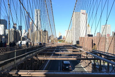 People at brooklyn bridge by cityscape against sky