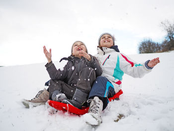 Playful siblings tobogganing on snow during winter