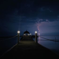 Illuminated pier on sea against sky at night
